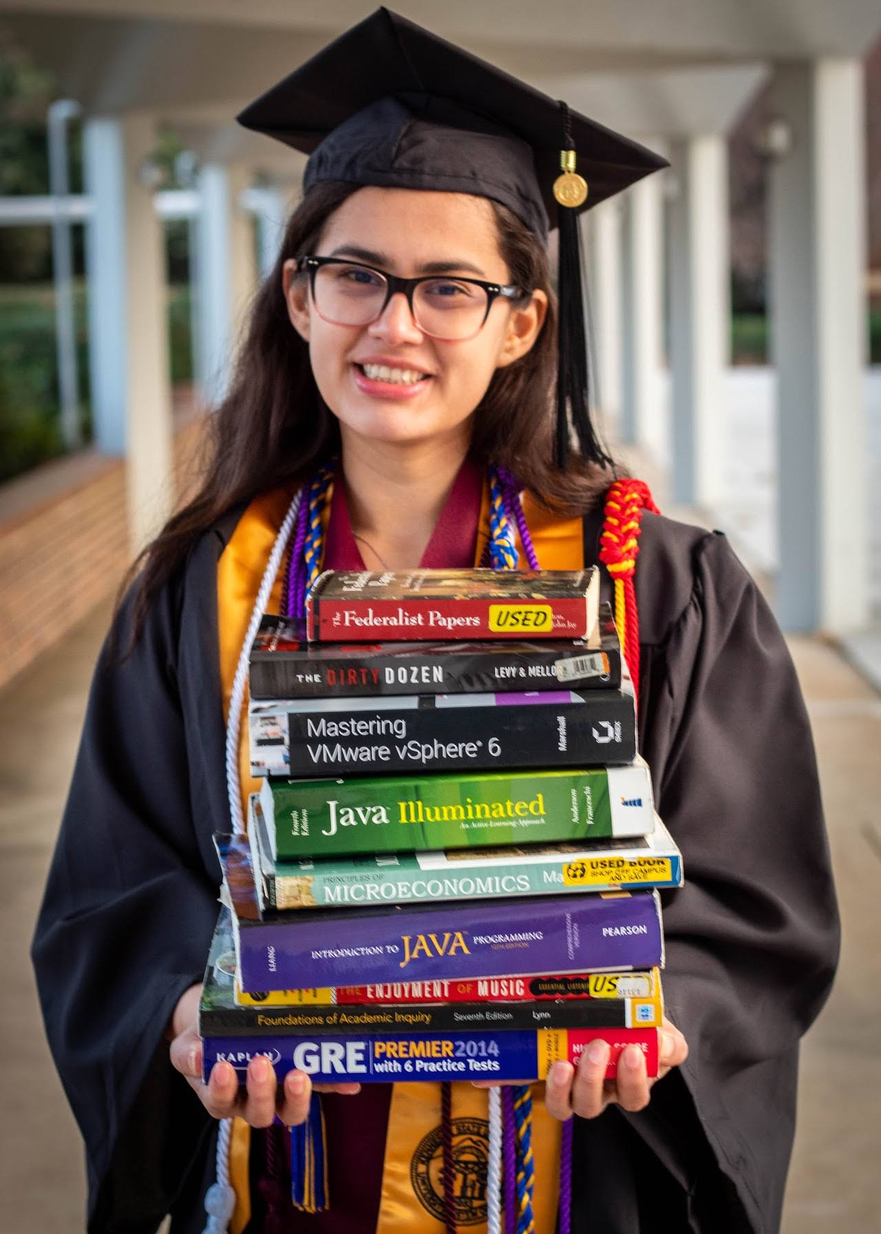 How to write a resume for your first job after college. Young women in cap and gown with books in her hand.